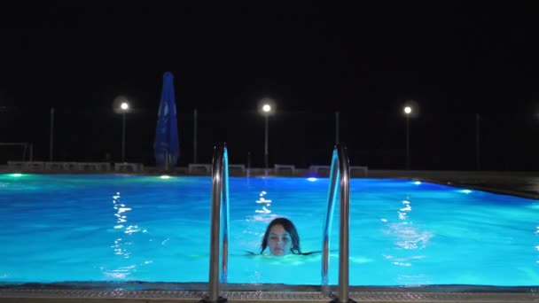 Sexy corpo giovane donna in costume da bagno esce di acqua colorata tenuta a scala di piscina in serata — Video Stock