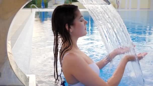 Disfrutar de la mujer joven en cascada refrescante en la piscina al aire libre en el descanso de verano — Vídeos de Stock