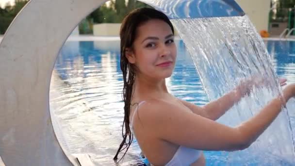 Hydroterapi för ung kvinna i baddräkt under konstgjort vattenfall i poolen — Stockvideo
