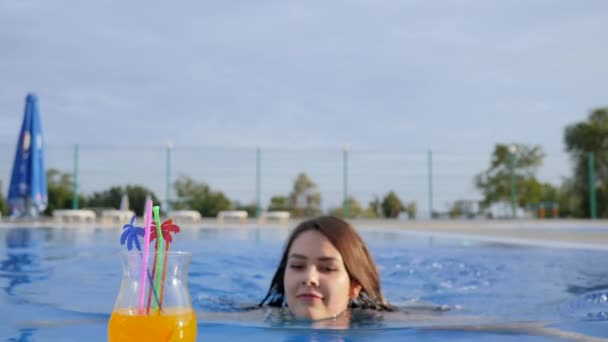 Piękna kobieta pływanie w niebieskim basenie i pić kolorowy koktajl i dając kciuki w górę na zewnątrz — Wideo stockowe