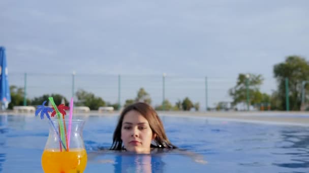Chica beber colorido cóctel y dar pulgares hacia arriba en la piscina en el cielo de fondo en vacaciones de verano — Vídeos de Stock
