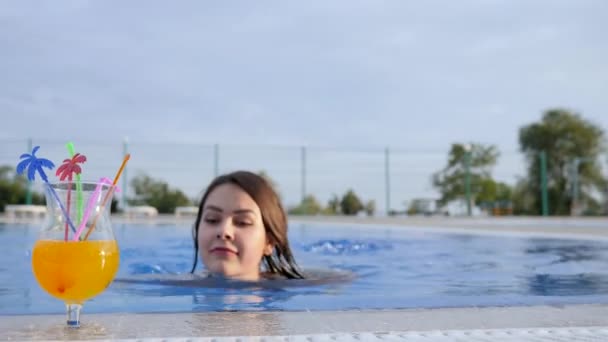 Позитивный жест молодой женщины, пьющей цветной напиток в бассейне на открытом воздухе — стоковое видео