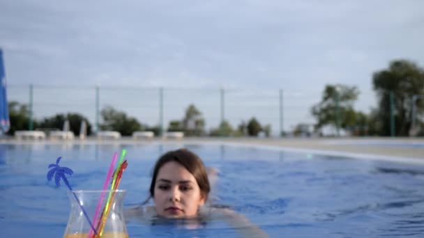 Молода жінка п'є алкогольні напої та відпочиває в літньому басейні на відкритому повітрі у відпустці — стокове відео