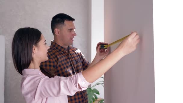 Appartement reparatie, jonge vrouw en man met tape maatregel in de hand doen renovatie in nieuwe huisvesting — Stockvideo