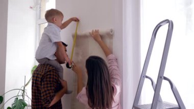 Odanın yenilenmesi, genç anne ve baba omuzları üzerinde çocuk duvar kağıdını yapıştırıyor.