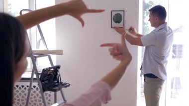 Yeniden dekore eden, güzel bir adam duvara resim asar. Kadın ise parmaklarıyla çerçeve yapar ve duvarları süslemeye karar verir.