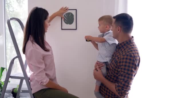 Decorate interior, nice kid with measuring roulette helps parents make repairs in apartment and hang picture — Stock Footage Decorate interior, nice kid with measuring roulette helps parents make repairs in apartment and hang picture Stock Footage