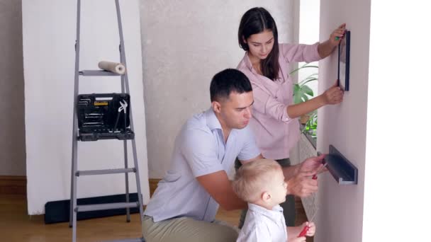 Padre enseña a su hijo pequeño a atornillar estante a pared con destornillador durante la reparación de apartamento — Vídeos de Stock