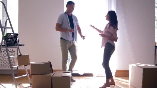 Vida feliz na nova casa após reparos, namorado alegre Com menina dança alegremente durante a mudança para o apartamento com caixas de papelão no chão — Vídeo de Stock