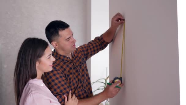 Felices propietarios de casas nuevas con cinta métrica haciendo renovación en la habitación y comunicarse — Vídeo de stock