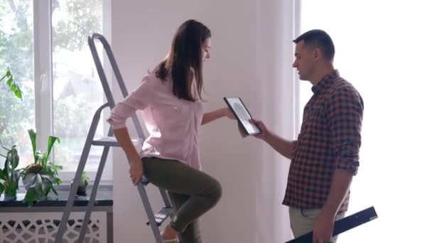 Home renovation, beautiful Lovers hang picture and shelf on white wall using ladder in apartment — Stock Footage Home renovation, beautiful Lovers hang picture and shelf on white wall using ladder in apartment Stock Footage
