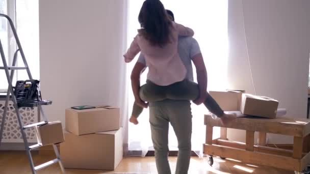 Housewarming, gelukkig Lovers is het hebben van plezier en vriendje is het dragen van meisje terug tussen de dozen tijdens het verhuizen naar appartement — Stockvideo