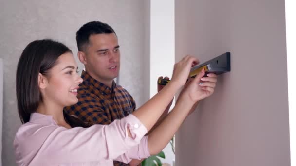 Married couple hanging shelf on wall with tape measure in arms during repairs in accommodation — Stock Video