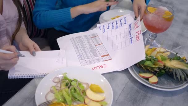 Диетолог консультирует женщин-клиентов по вопросам питания и подсчитывает калории на листе бумаги во время здорового ужина — стоковое видео