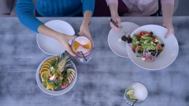 Питание и досуг, вид сверху на девушек, обедающих и подающих салат за столом со здоровой пищей и напитками — стоковое видео