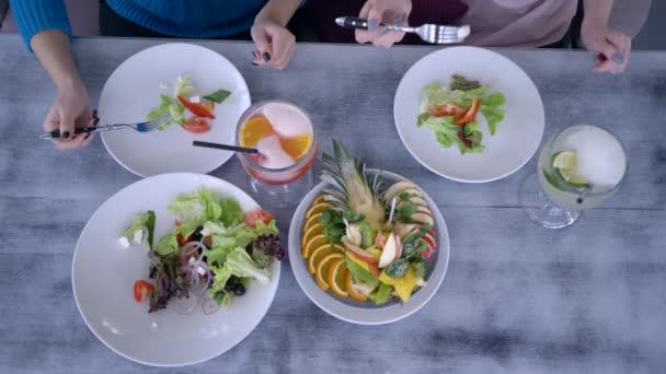 zdravé jídlo a džus v brýlích na stole, dívky drží v ruce vidličky a jí řecký salát z talířů