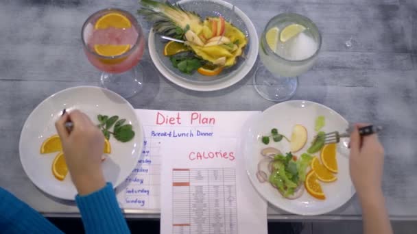 Comida vegana saludable, las niñas comen fruta de platos sentados en la mesa con la tabla de calorías y plan de dieta — Vídeos de Stock