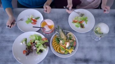 Sağlıklı yemek ve bardak suyu olan bir masa. Tabakların yanında çatallı insanları yiyen eller.