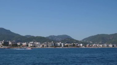 Deniz manzarası, mavi Akdeniz kıyısında yüzen motorlu tekneler şehir ve dağların arkasında