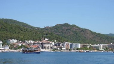 Turist teknesi mavi Akdeniz kıyısında yeşil dağlarla birlikte şehrin arka planında yüzüyor.
