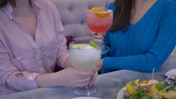 Sabrosa dieta, hermosas chicas felices comunicarse y beber jugo a través de una paja de grandes vasos en el restaurante — Vídeos de Stock