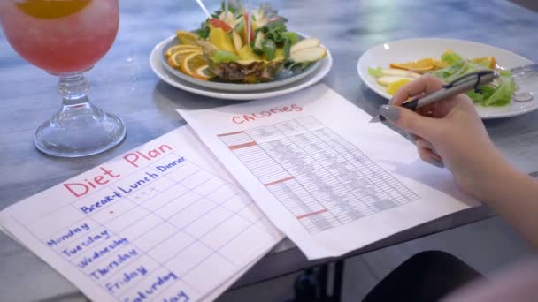 Dieta gustosa, nutrizionista femminile alla ricerca di calorie in lista seduta a tavola con punch e frutta in piatto — Video Stock