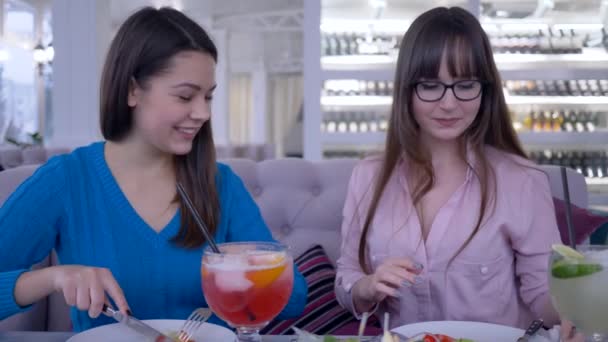 Tiempo para comer, las mujeres jóvenes se comunican y cortan ensalada con tenedor y cuchillo en las manos durante la dieta en la cafetería — Vídeos de Stock