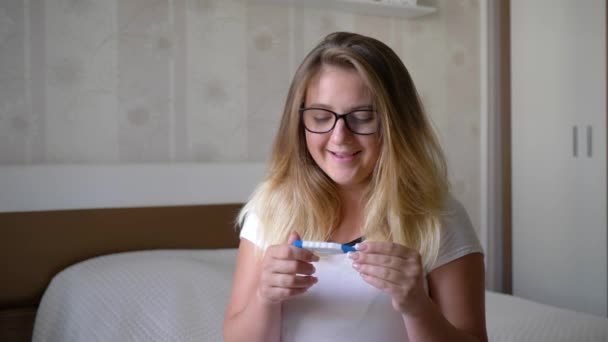 Unexpected pregnancy, happy young woman with birth control test sits on the edge of bed at home — Stock Video