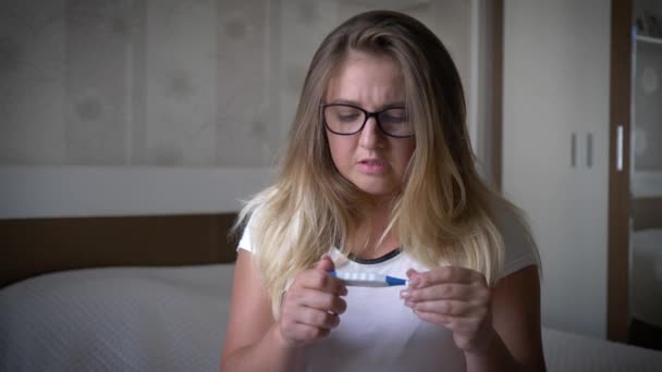 Unhappy pregnant woman, worried girl looks at pregnancy test sitting on edge of the bed in room — Stock Video