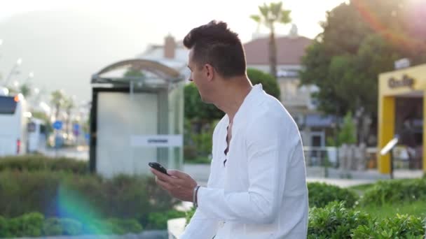 Emocional mostrando sucesso, homem bonito usa telefone celular rosto surpreso ao ar livre — Vídeo de Stock