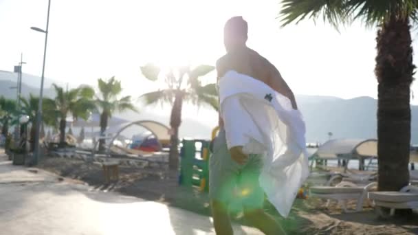 Gelukkige reiziger op de vlucht doet zijn kleren uit en zwaait met wit shirt buiten in backlight op vakantie — Stockvideo
