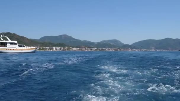 Mer Méditerranée, bateau flottant au bord de l'eau bleue sur fond de paysage urbain avec des montagnes vertes — Video