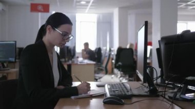 Kötü iş, gözlüklü somurtkan kız bilgisayarda çalışır ve not defterine not alır.