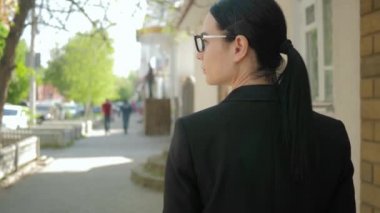 Ciddi iş kadını şehir caddesinde yürüyor ve dışarıdakinden daha çok düşünüyor, ağır çekim.