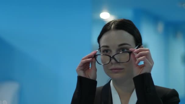 Mujer joven y cansada en el baño público se quita las gafas y se mira en el espejo — Vídeos de Stock