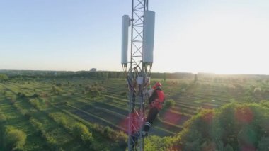 Telekomünikasyon kulesinin hava görüntüsü, güvenlik yeleği ve kasketli teknisyen cep telefonu anteninin üstünde cep telefonu kullanıyor.