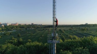 Tehlikeli iş, sert şapkalı telsiz teknisyeni. Telekomünikasyon kulesinden inin. Güzel manzaranın arka planında destek var.