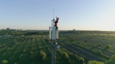Cihazı olan mühendis, günbatımlı mavi gökyüzünün arka planındaki radyo telekomünikasyon kulesinde mobil bir iletişim kurdu.
