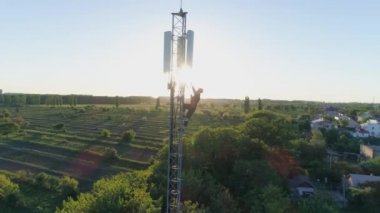Anten iletişim kulesindeki yüksek irtifa işçisi mobil bir arama yapıyor ve telekomünikasyon kulesinin uzaktan kumandalı görüntüsü olan güneş ışığında baş parmağını gösteriyor.