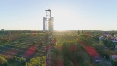 Bakım işçisi, günbatımının arka planındaki güvenlik ekipmanları ve hücresel antenin drone görüntüsünü kullanarak iletişim kulesinde onarım yapıyor.