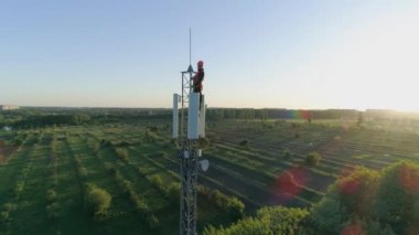 Hücresel antenin tepesindeki mutlu adam, radyo telekomünikasyon kulesindeki teknisyen gökyüzünün arka planında başparmağıyla elini kaldırıyor.