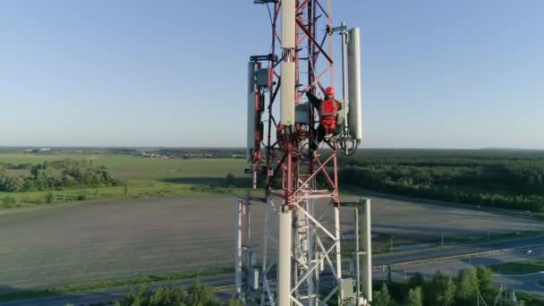 Vista aérea a la antena celular, maestro de radio trabajando en torre de telecomunicaciones vestido con sombrero duro — Vídeo de stock