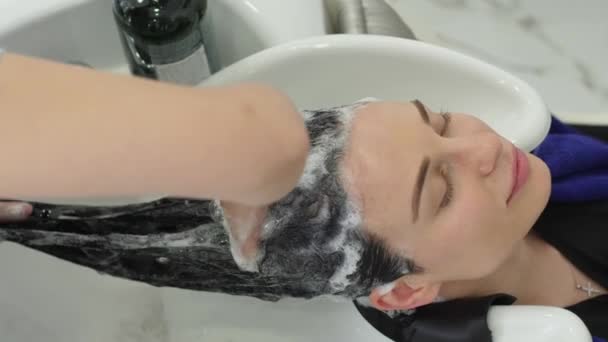 긴 머리를 한 갈색 머리 소녀가 샴푸로 머리를 씻기 위해 미용실을 찾는 여성 시술 — 비디오