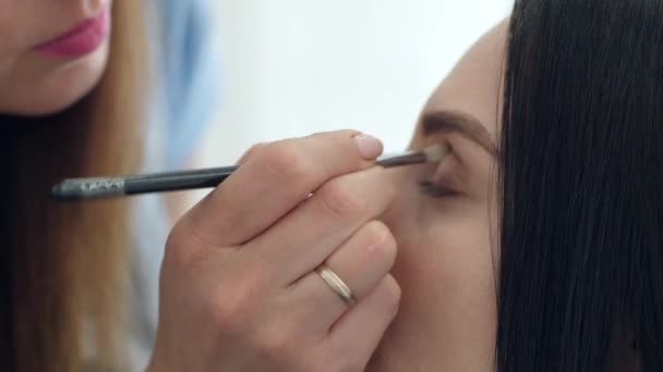 Visagiste con el pincel especial hace el maquillaje profesional a los ojos del modelo en el salón de belleza — Vídeo de stock