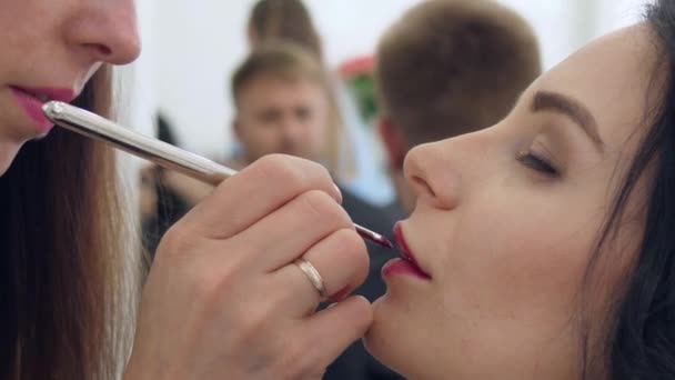 Профессиональный макияж, молодой человек смотрит на процесс краски губ женщины в салоне красоты — стоковое видео