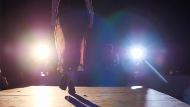Модель прогулянки на високих підборах в сукні йде на подіум у освітленні прожектора перед публікою — стокове відео