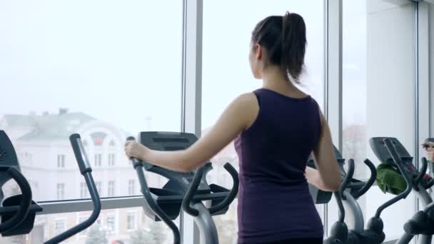 Atleta chica entrena los músculos de las piernas en simulador de deportes en el gimnasio con grandes ventanas — Vídeo de stock