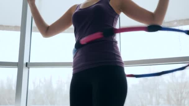 Studio fitness, kształtna dziewczyna obraca pierścień w pasie w centrum sportowym na tle dużych okien — Wideo stockowe