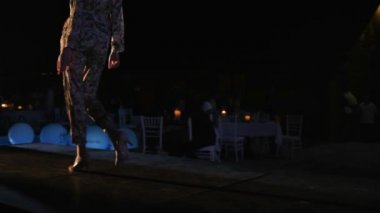 Gülümseyen bir manken şık bir takım elbise içinde moda gecesinde podyumda yürüyor.