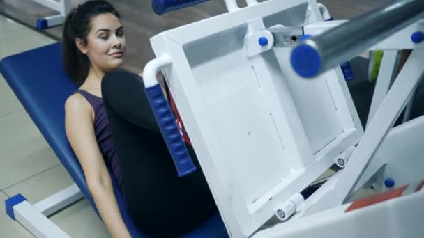 Actividades deportivas, chica sonriente están entrenando acostado en las piernas máquina de prensa en el gimnasio — Vídeo de stock